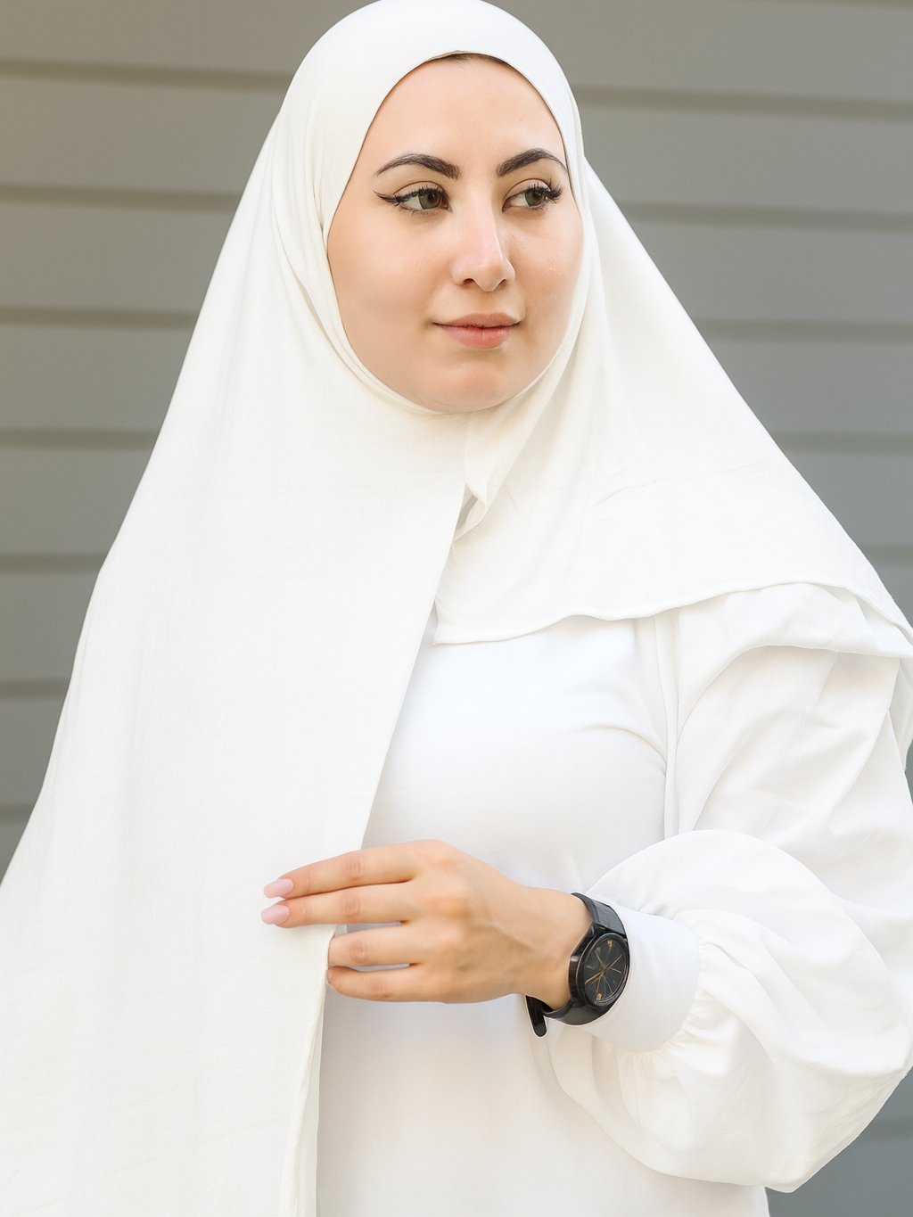Woman wearing a white hijab and white outfit against a neutral background