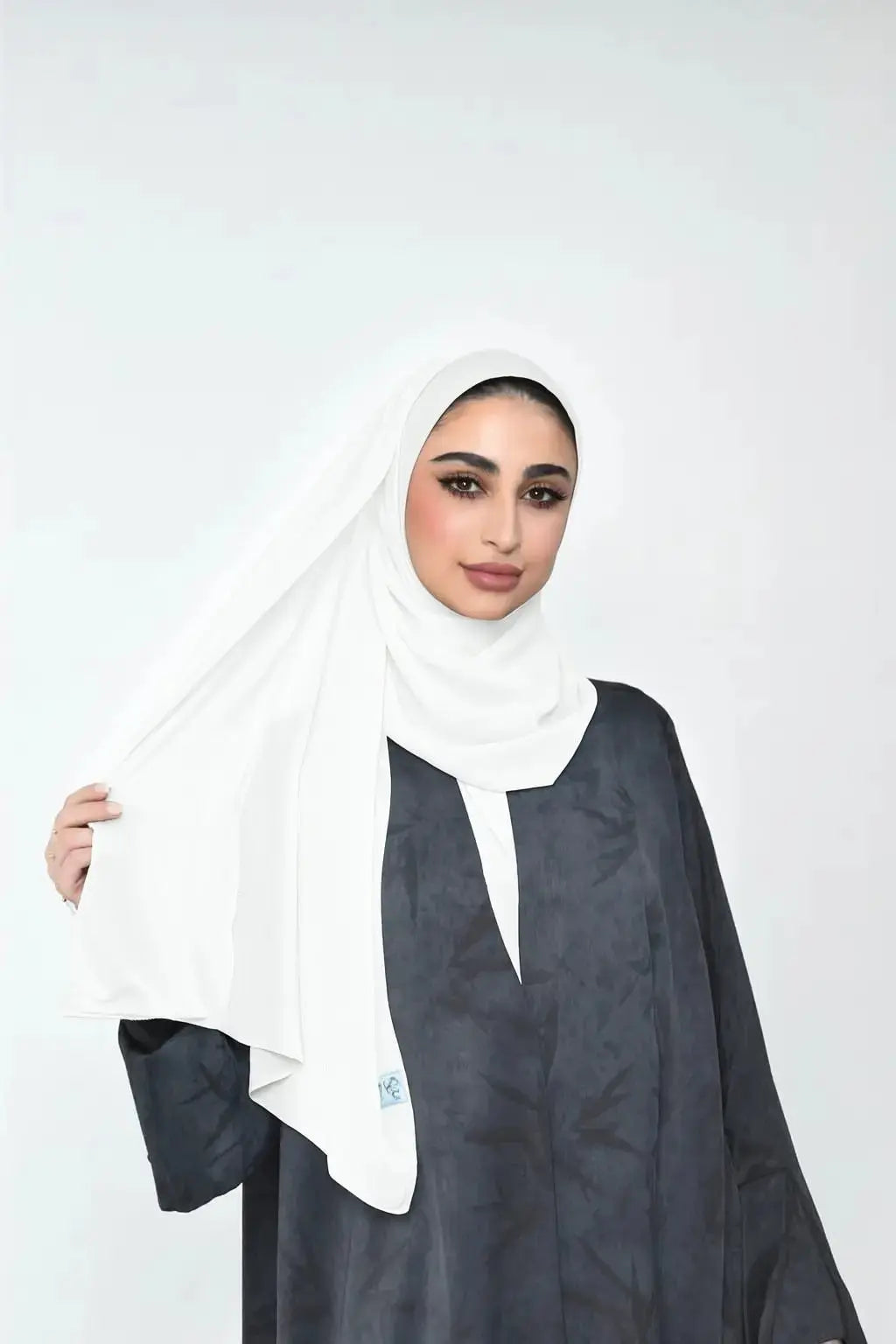 Woman wearing a white hijab and dark outfit on a white background