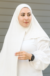 Woman wearing a white hijab and white outfit against a neutral background